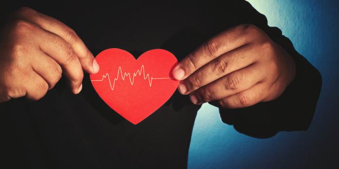 A person in a black sweater holds a red heart cut-out over their chest.