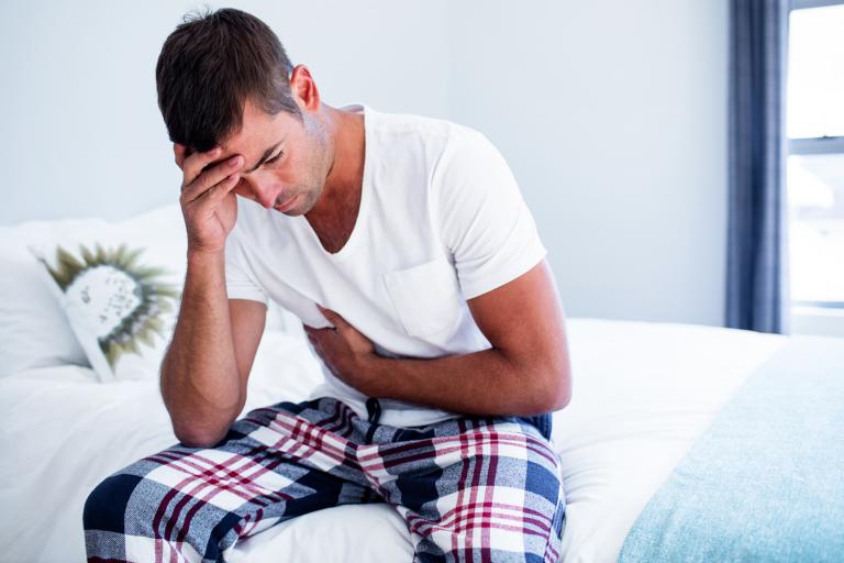 A man sitting on his bed with stomach discomfort.